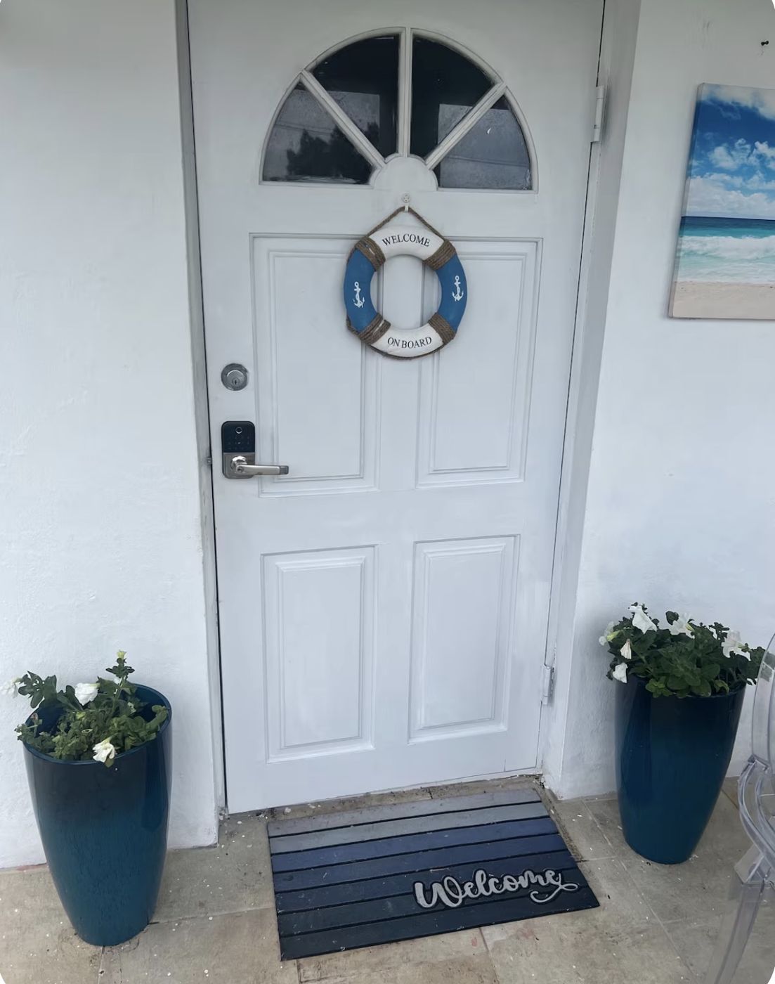 White front door with a Welcome On Board life ring and blue planters