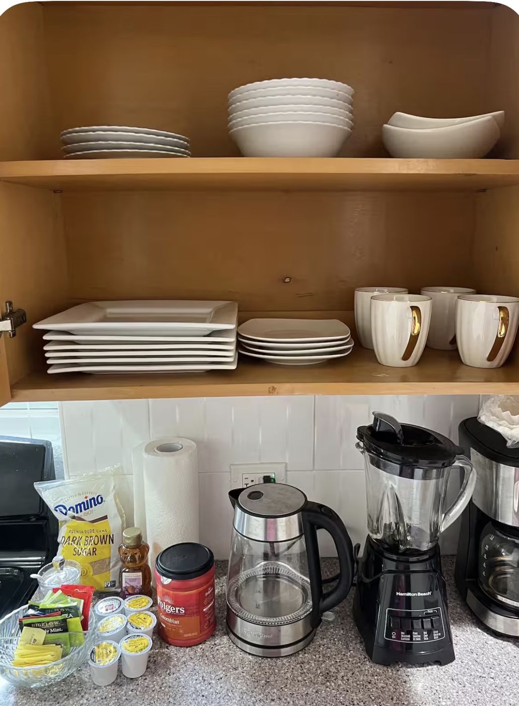 Cupboard of white dishes above a coffee station with kettle, blender and coffee maker