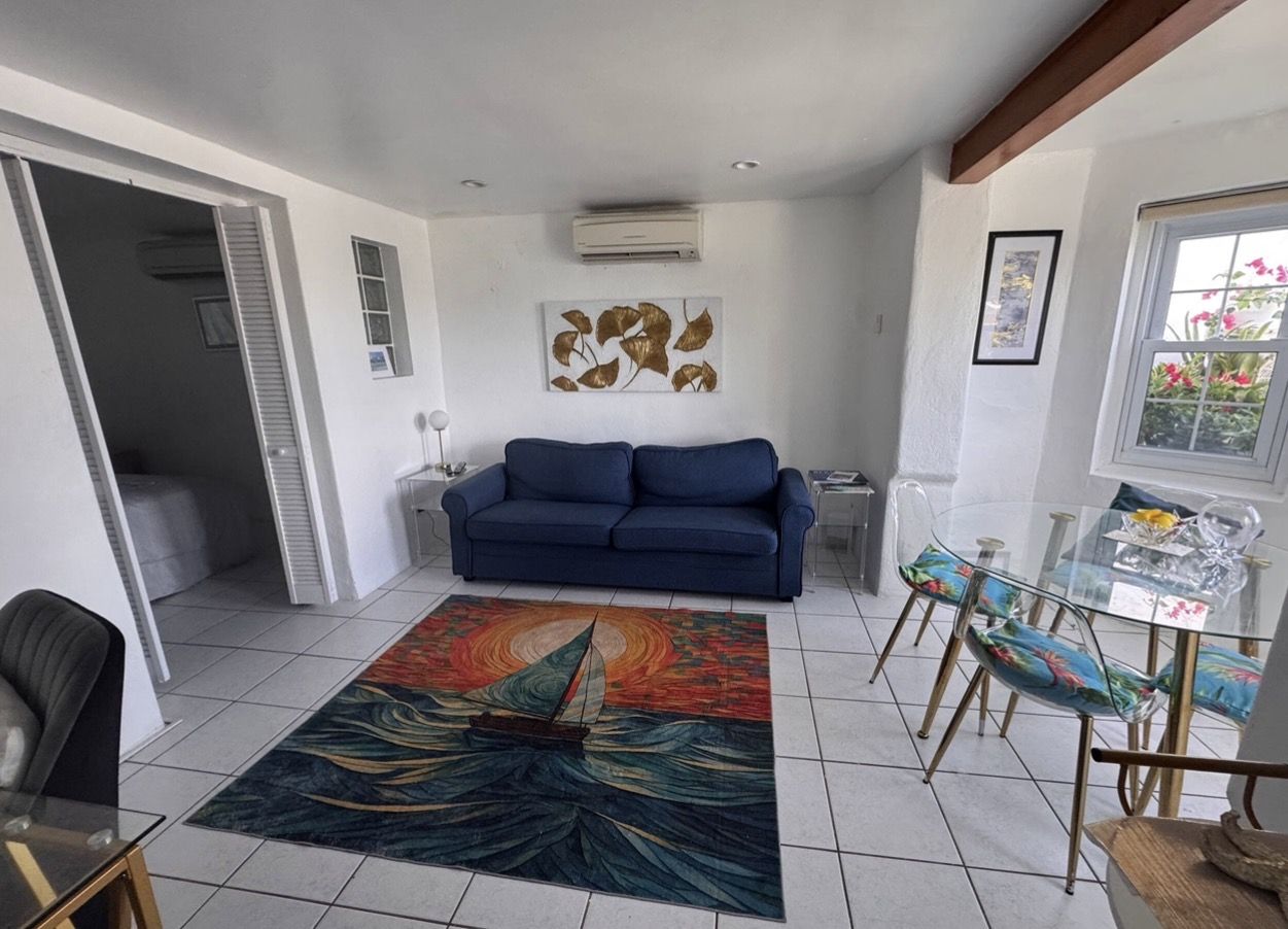 Living room with navy queen pull-out sofa bed, sailboat sunset rug and glass dining table by the window
