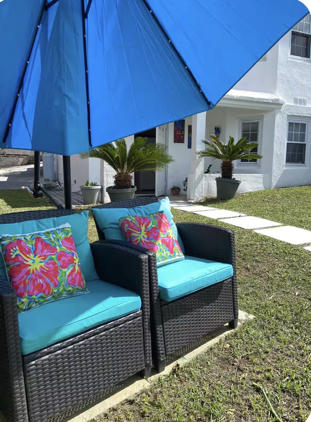 Wicker chairs with turquoise cushions and hibiscus pillows under a blue umbrella
